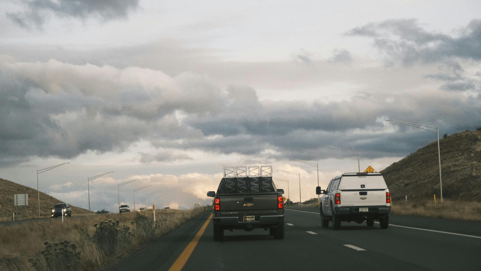 Deux camionnettes roulent sur une route panoramique sous un ciel nuageux.